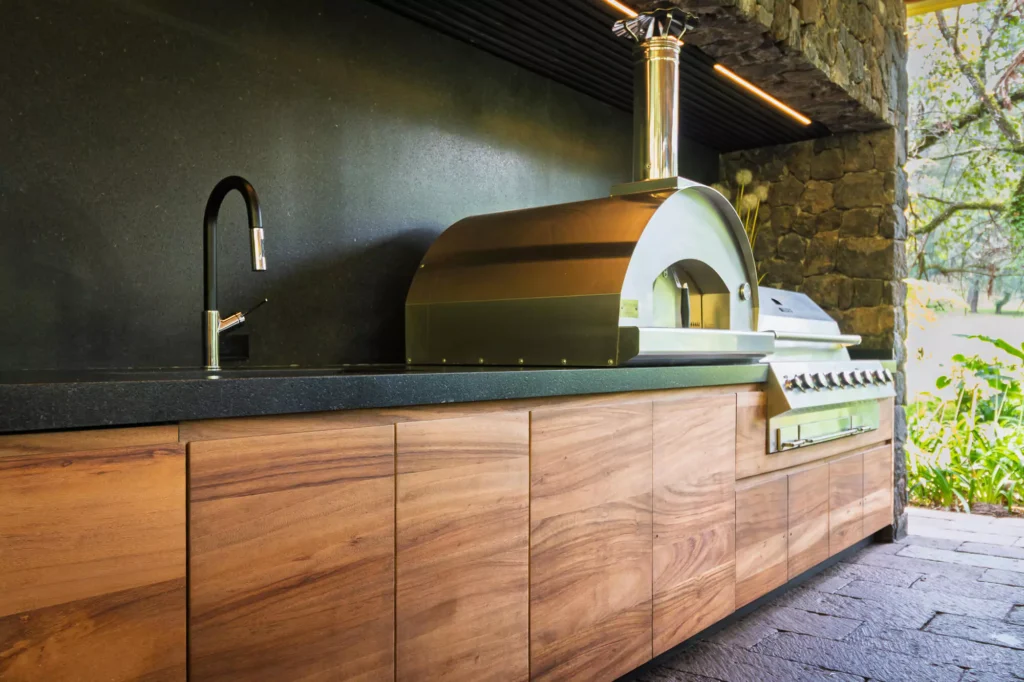 Wood and stone outdoor kitchen surrounded by greenery, designed by Vitelier at Club de Golf Avándaro, State of Mexico.