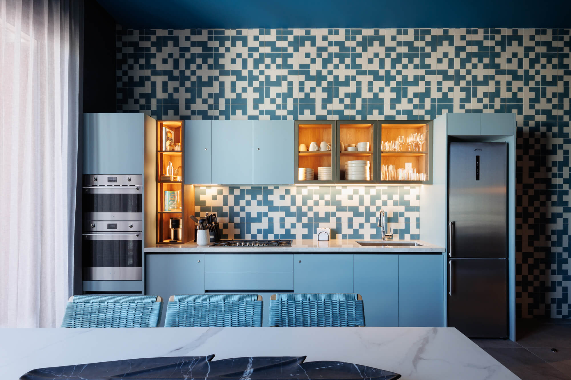 Cocina en línea azul con blanco con muro de mosaicos de efecto pixel.