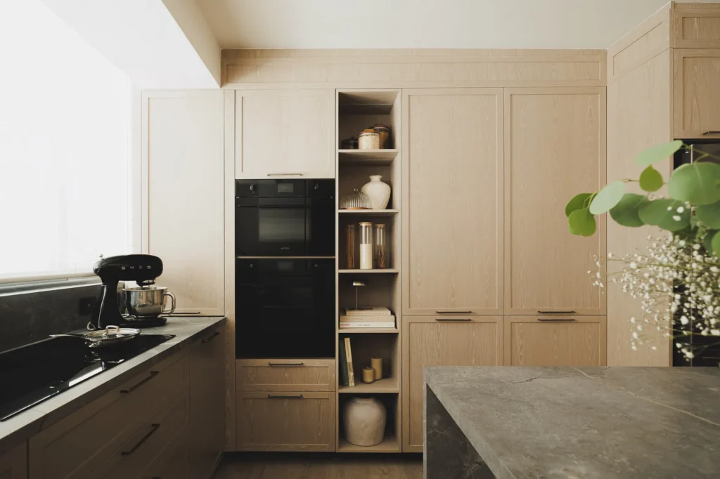 Oven tower, open module, and panel-ready appliances in a patina wood kitchen with sintered stone countertop