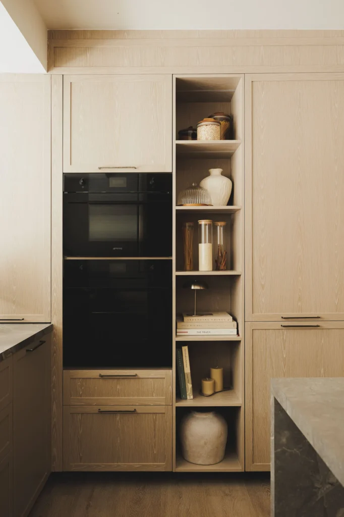 Oven tower, open module, and panel-ready appliances in a patina wood kitchen with sintered stone countertop