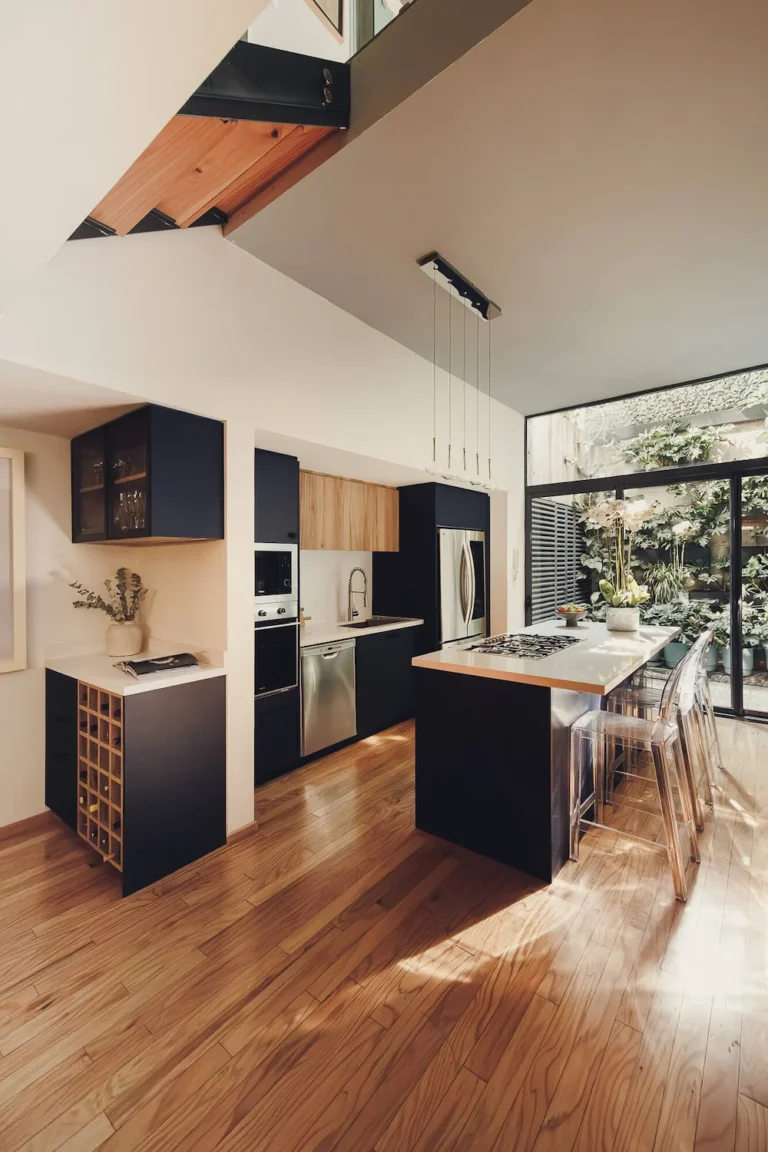 Cocina abierta con isla central, frentes de melamina azul índigo y muro de cristal con jardín interior — diseño de cocinas en la Roma, CDMX por Vitelier