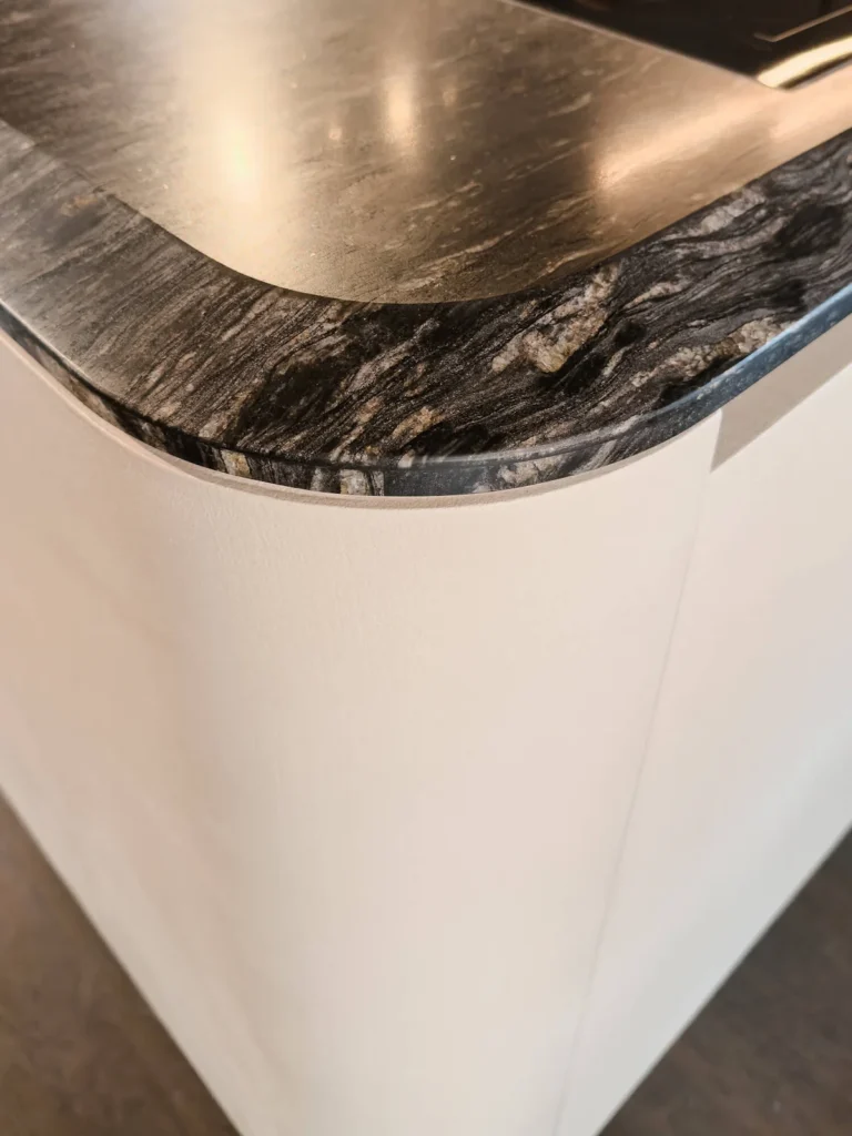 Isla Boffi Cove de Zaha Hadid Design: base curva en Corian blanco con cubierta de mármol oscuro veteado.