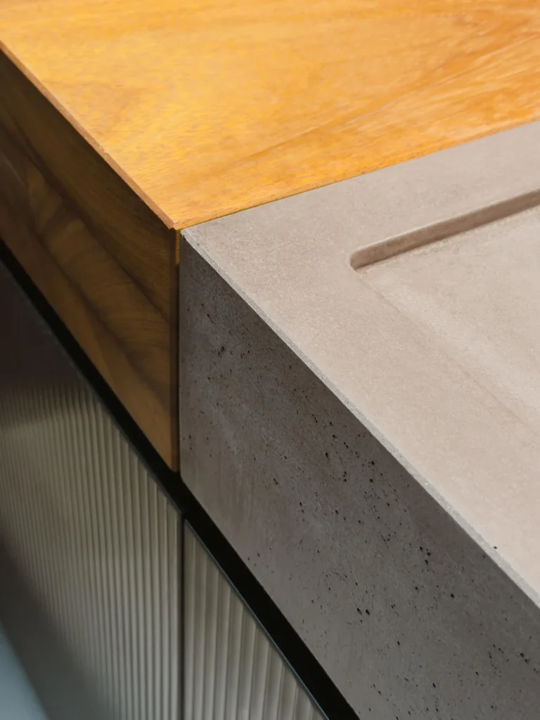 Detalle de esquina en cocina Evoluta OTOK: cubierta de concreto con jaladera incisa y costado de madera maciza sobre frentes acanalados.