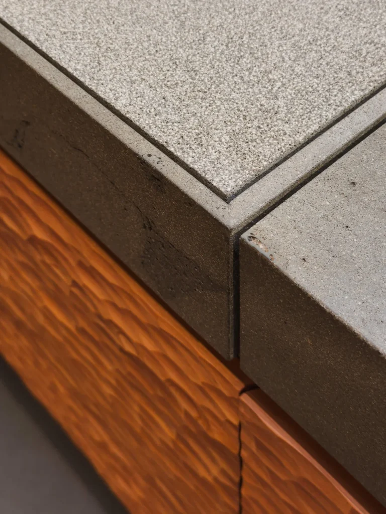 Detalle de la isla Fisher & Paykel Nature–Ritual: arista entre cubierta en basalto volcánico neozelandés y frente de cajón en madera de tōtara tallada con textura ondulada hecha a mano.