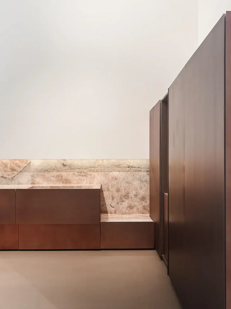 Cocina Minotti Cucine con gabinetes en acabado cobre y backsplash de cuarcita rosa retroiluminada, exhibida en EuroCucina 2026.