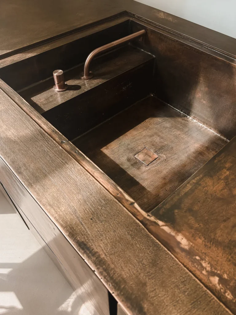 Detalle de la cubierta en bronce fundido de la cocina Terra de Minotti Cucine (Claudio Silvestrin), con tarja integrada tallada en el mismo volumen y grifería en bronce a tono, EuroCucina 2026.