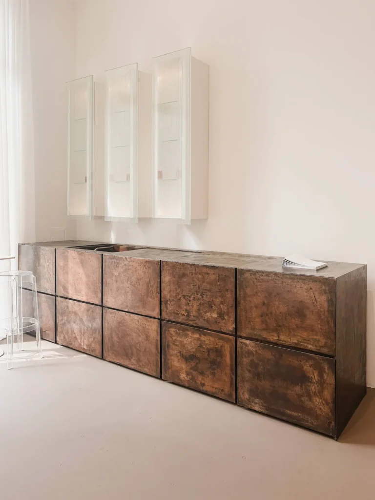 Isla de cocina Terra de Minotti Cucine (Claudio Silvestrin) en bronce fundido, con módulos altos colgados al fondo, vista en su showroom durante EuroCucina 2026.