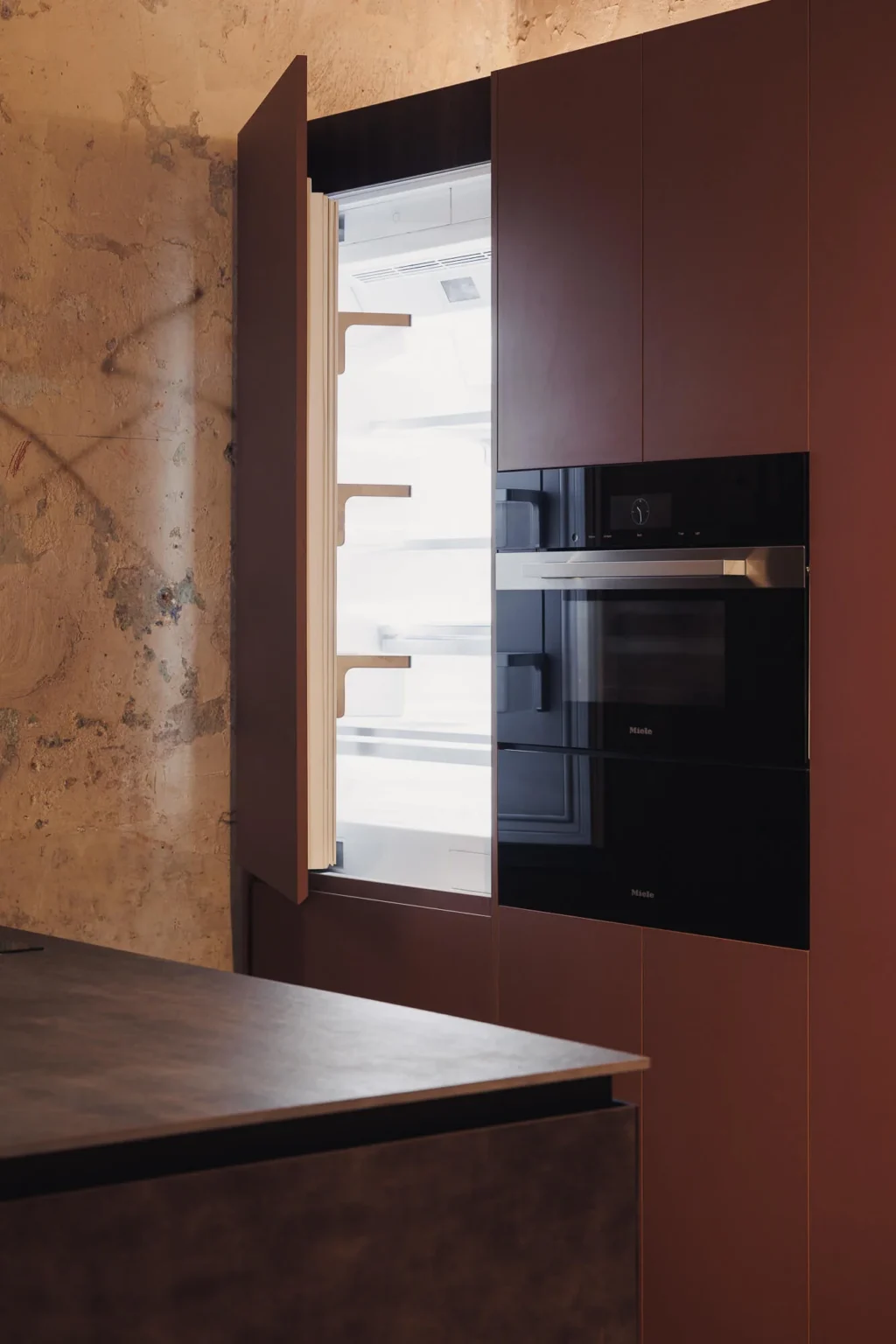 Miele Combi MasterCool refrigerator with panel-ready Interforest copper laminate door open, next to the Miele steam oven — Proyecto Público Prim.