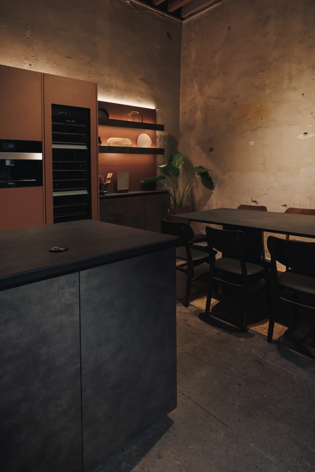 Central island of the Casa Taittinger kitchen clad in aged metallic sheet and open display cabinet with copper backing, over the original stone floor — design by Vitelier at Proyecto Público Prim.