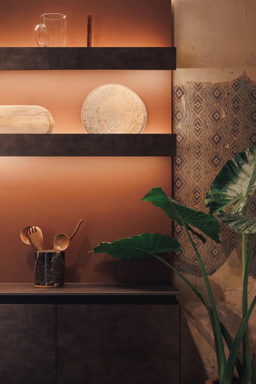 Open display cabinet with shelves and lit copper backing, next to a fragment of antique mosaic preserved on the wall — Casa Taittinger kitchen at Proyecto Público Prim by Vitelier.