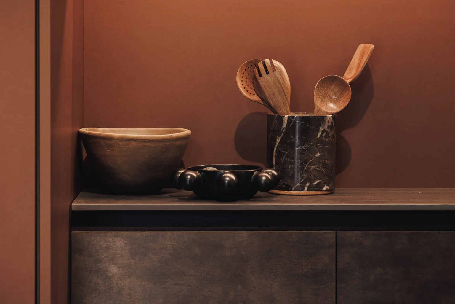 Clay vessel, marble mortar and wooden utensils over Dekton Bromo countertop and Interforest copper backing — open display cabinet detail.
