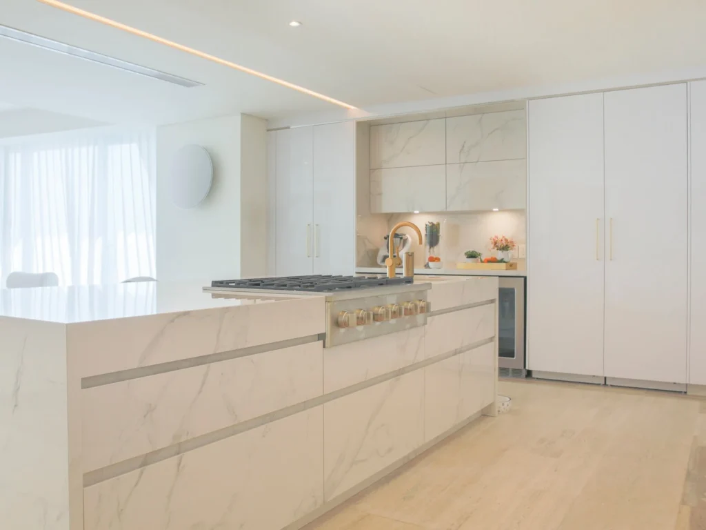Isla de cocina recubierta en Dekton Natura con parrilla de gas empotrada y grifería dorada en departamento de Acapulco.
