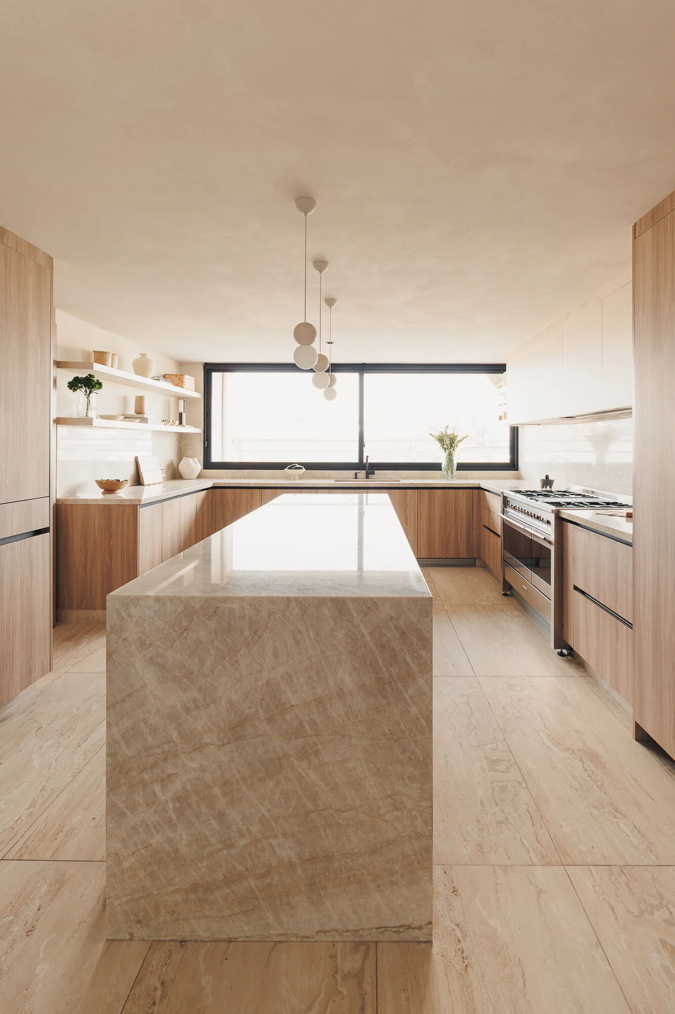 Vista frontal de cocina cerrada con isla de cuarcita, gabinetes de Maple Samsara, repisas flotantes y ventanal horizontal con marco negro — diseño de cocinas en Ciudad de México por Vitelier.
