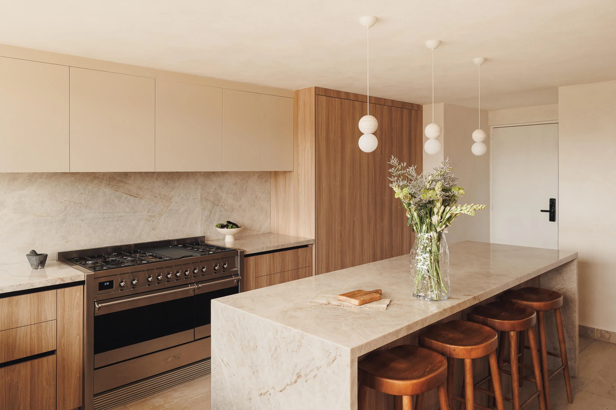 Vista panorámica de cocina cerrada con estufa Smeg profesional, gabinetes Cashmere y Maple Samsara, isla de cuarcita Taj Mahal con bancos de madera — diseño de cocinas en CDMX por Vitelier.
