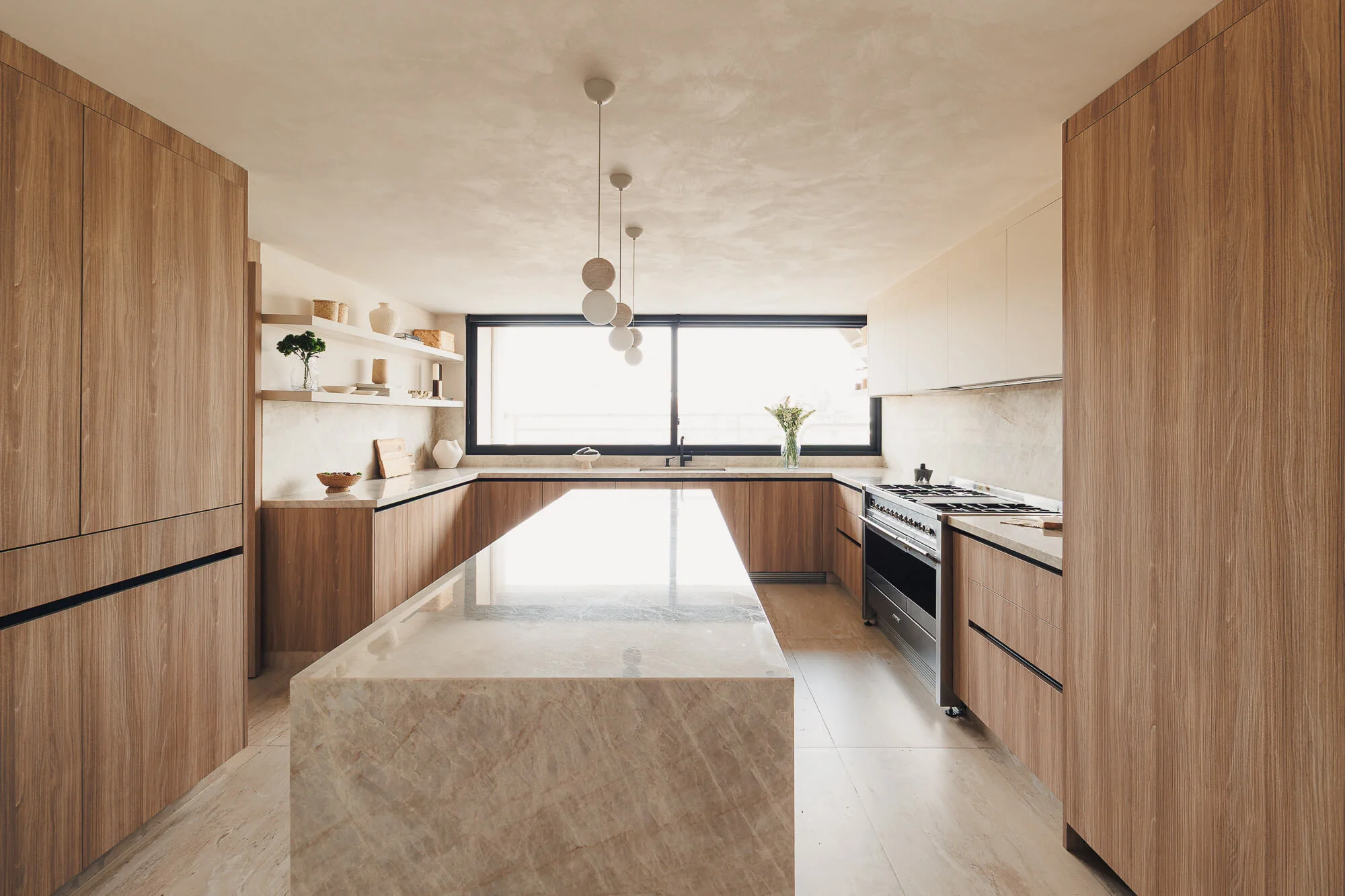 Vista simétrica de cocina cerrada de 23 m² con isla de cuarcita, torre de almacenamiento en Maple, repisas flotantes y luminarias esféricas — Vitelier, estudio de diseño de cocinas en CDMX.