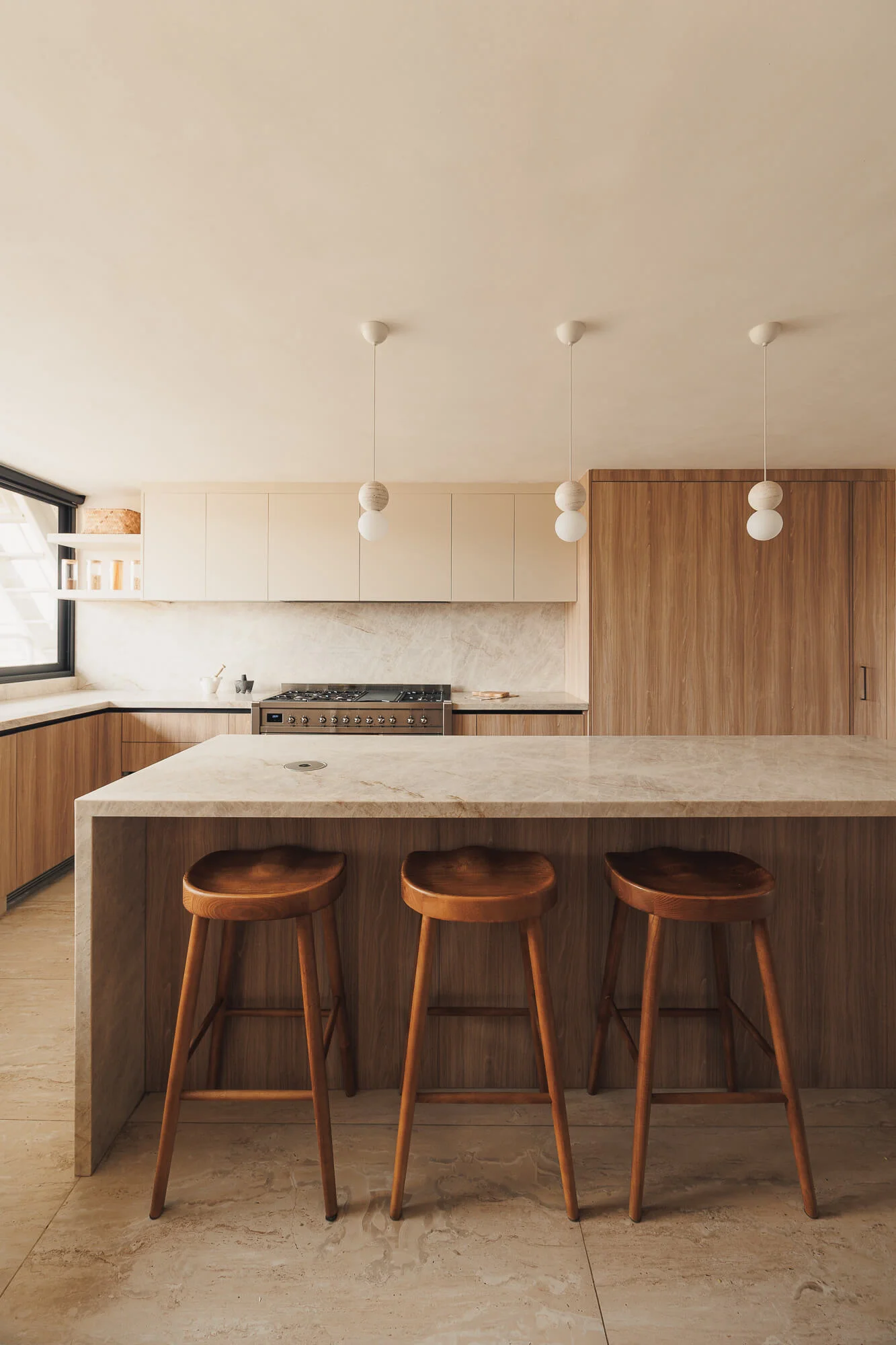 Isla central con cubierta de cuarcita Taj Mahal en cascada y tres bancos de madera maciza bajo luminarias esféricas — cocina de 23 m² diseñada por Vitelier en CDMX.