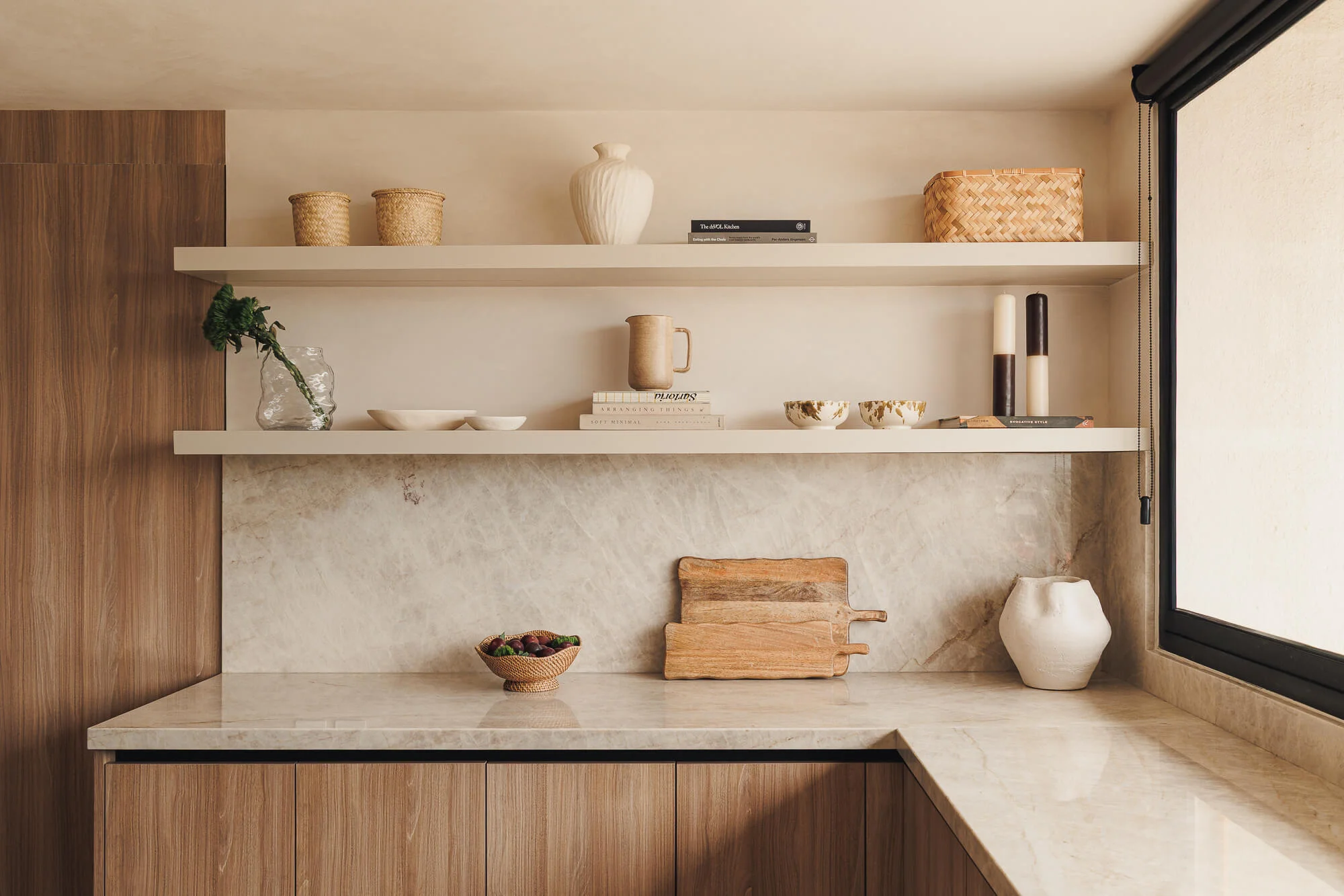 Repisas flotantes con cerámica, libros y cestas tejidas sobre backsplash continuo de cuarcita Taj Mahal y gabinetes inferiores Maple Samsara — detalle de cocina residencial Vitelier en CDMX.