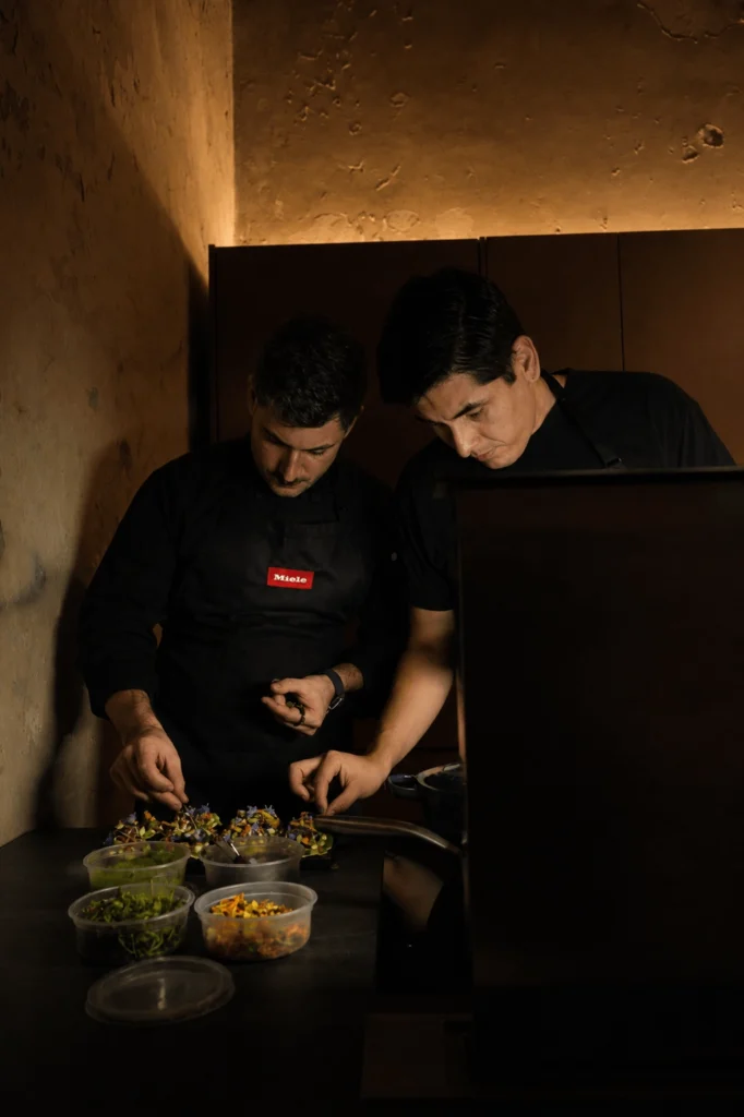 Dos chefs emplatando bocados con flores comestibles en la cocina Vitelier de Casa Taittinger